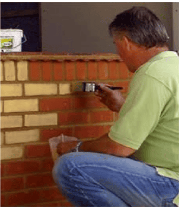 A person applying a stain or paint to a brick wall using a brush, demonstrating the process of transforming the brick’s appearance.