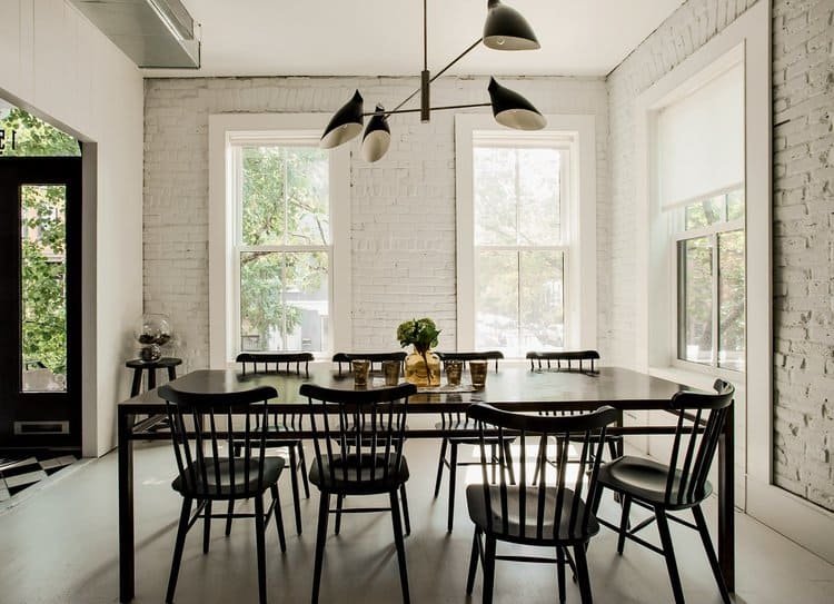A dining room with white-painted brick walls, featuring large windows and modern black furniture, creating a bright and stylish interior.