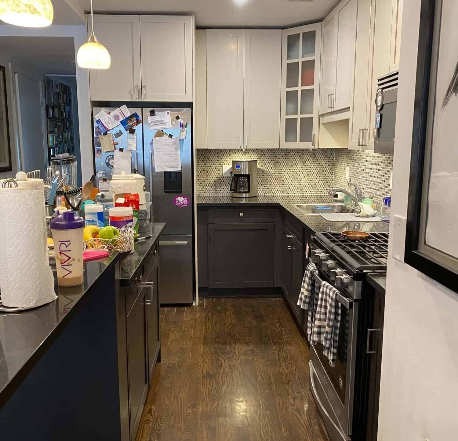 Kitchen with white upper cabinets, dark lower cabinets, a mosaic tile backsplash, and various items on the countertops.