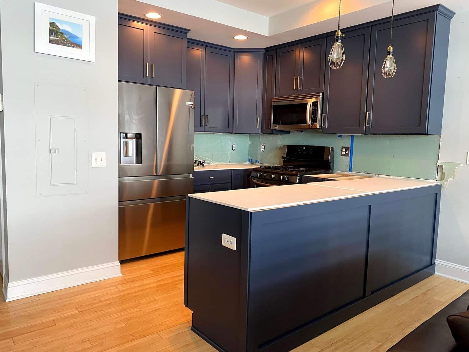 Kitchen with dark blue cabinets, stainless steel appliances, and pendant lighting over a partially finished countertop.