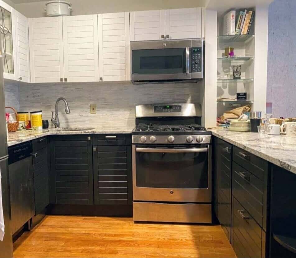 Kitchen with a mix of white upper cabinets and black lower cabinets, stainless steel appliances, and a marble backsplash.