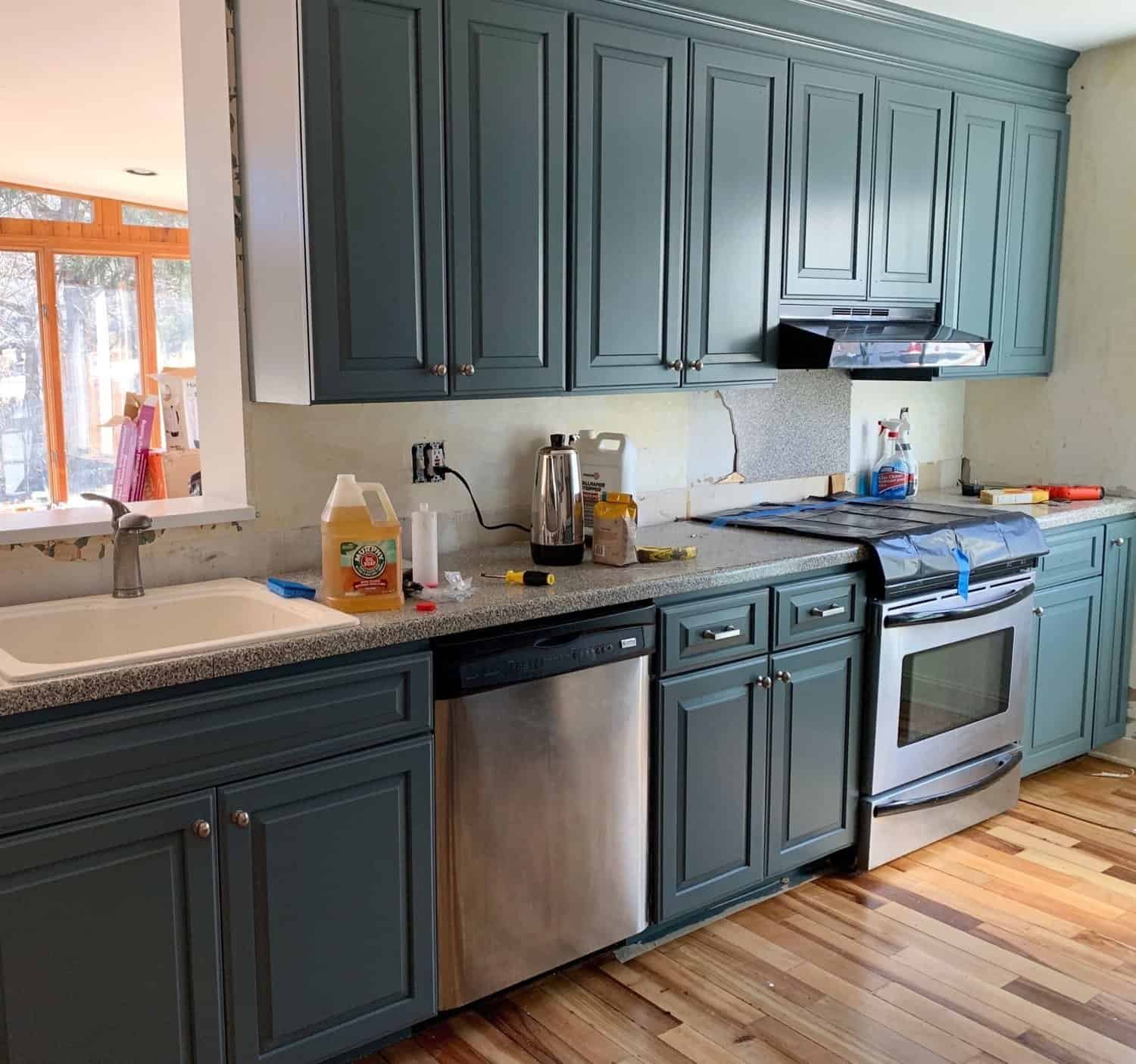 Kitchen with teal cabinets and stainless steel appliances, featuring a sink and tools on the countertop.