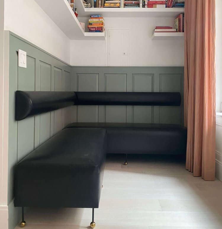 A finished nook with green wainscoting, black cushioned seating, and built-in bookshelves above.