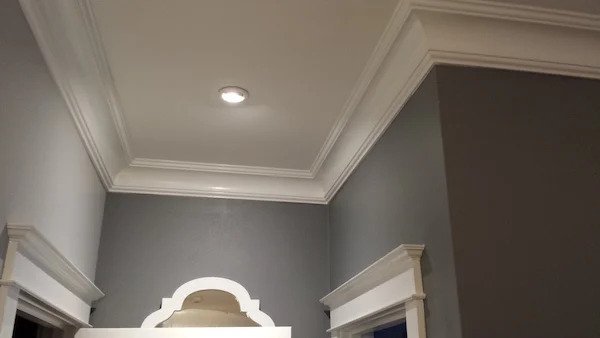White crown molding and trim installed in a room with gray walls, featuring a recessed ceiling light.