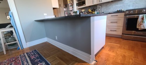 A kitchen island with freshly installed drywall, painted gray with white trim, blending seamlessly with the surrounding cabinetry and flooring.