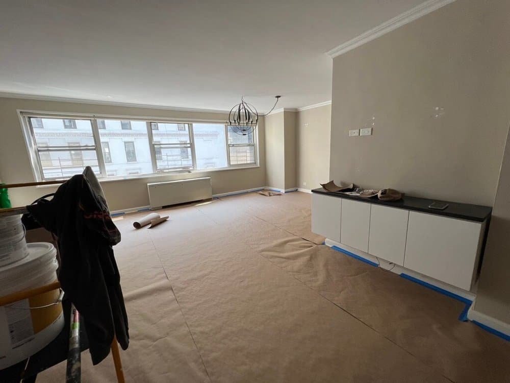 A large living room in the process of renovation with protective paper covering the floor and a cabinet fixed to the wall.