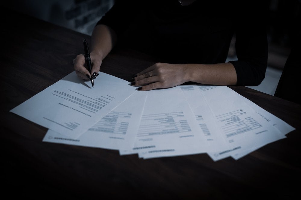 A person signing documents on a dark wooden table.