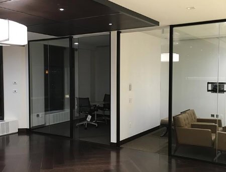 An office space with glass partitions and dark wood accents, featuring white walls and modern furnishings, creating a sleek and professional environment.