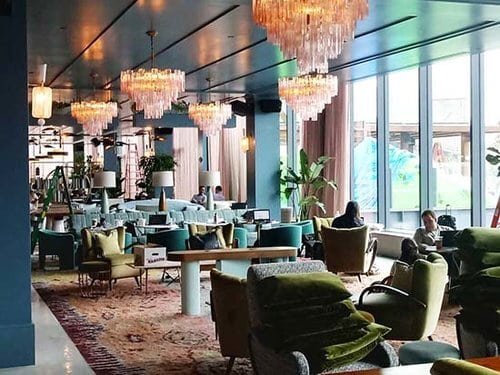 A chic, upscale restaurant lounge with elegant chandeliers, plush seating, and floor-to-ceiling windows allowing natural light to flood the space.
